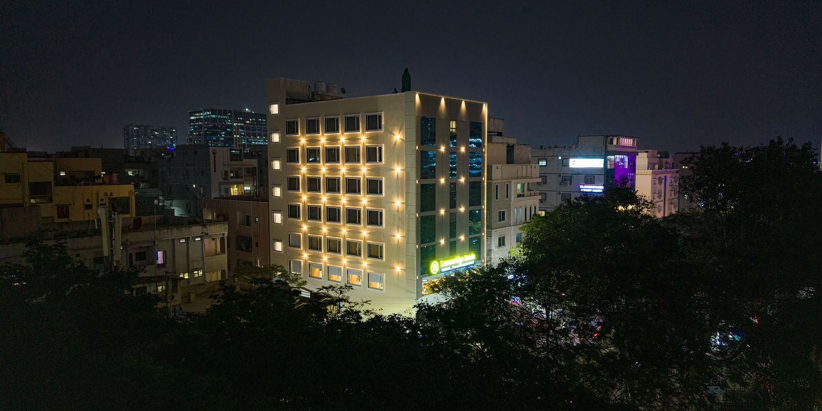 Lemonridge Hotels, KPHB | Exterior nighttime view of the hotel building, illuminated against the dark sky. Trees visible in foreground.